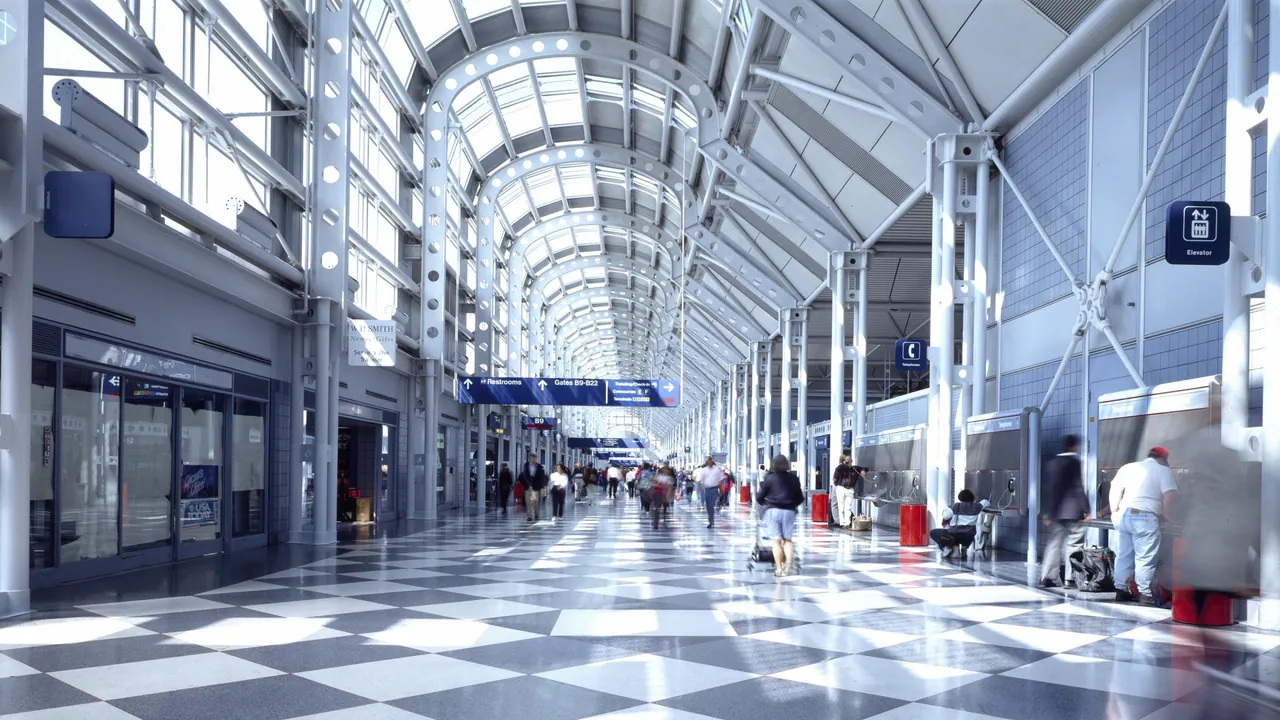A bright glass-roofed airport concourse with passengers moving between gates, signs, lifts, and seating areas
