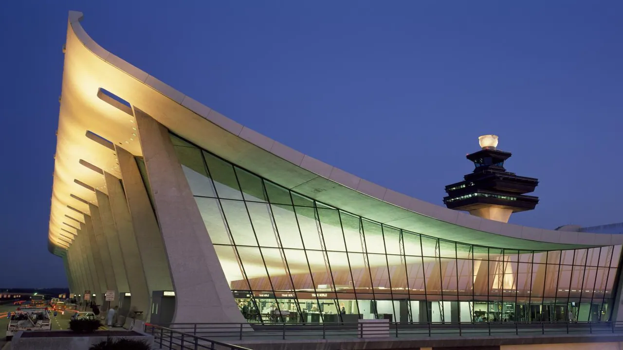 The sweeping concrete and glass terminal at Dulles Airport lit from within at dusk, its control tower against a deep blue sky