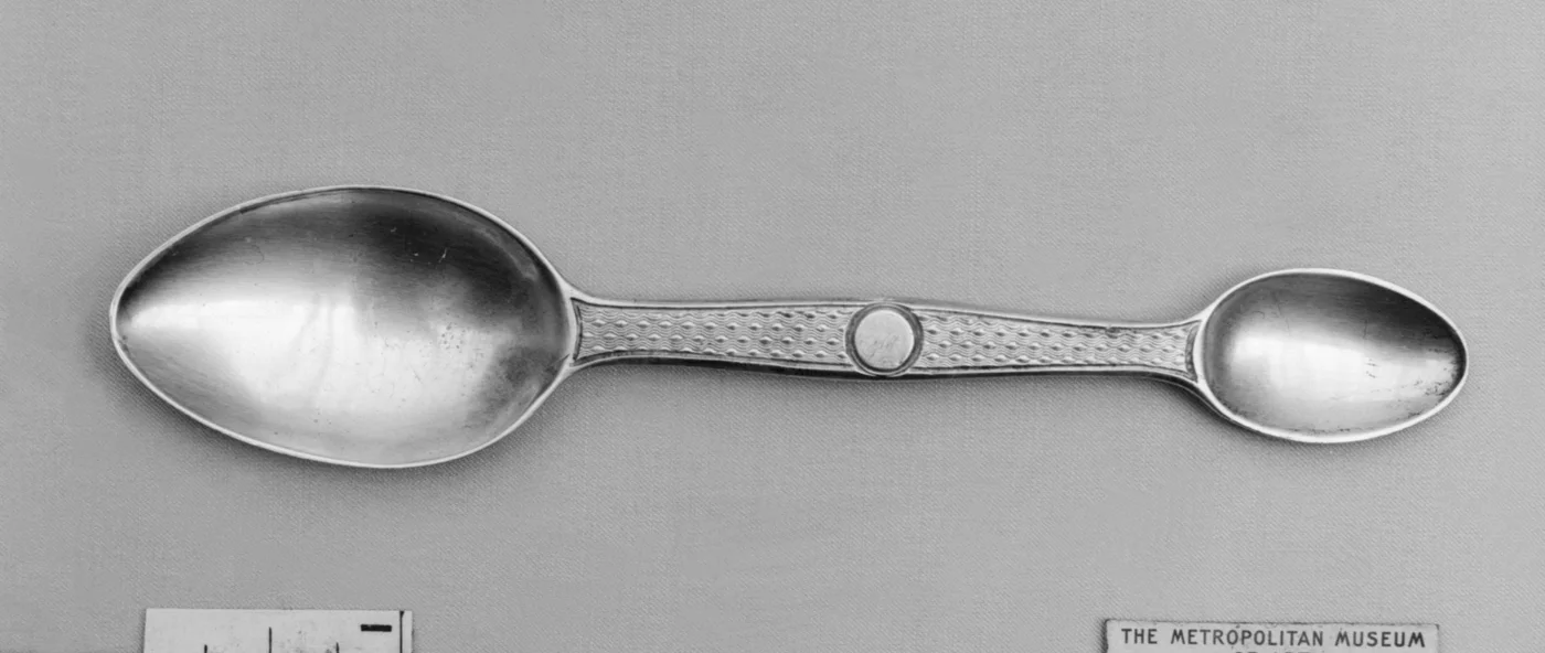 A long-handled nineteenth-century silver medicine spoon shown against a dark neutral background