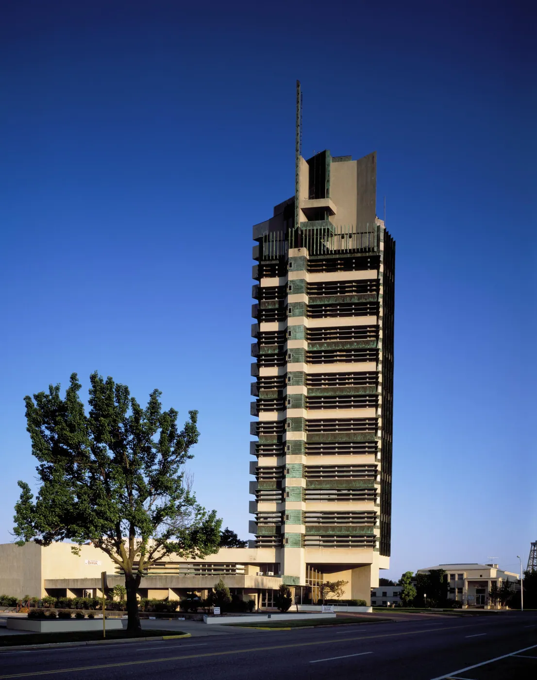 Frank Lloyd Wright's copper-trimmed Price Tower rising alone against a deep blue sky above a low building and a leafy tree