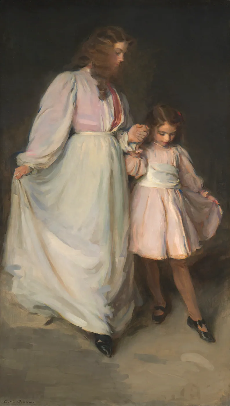 A young woman in a long white dress holds the hand of a small girl in pink as they step forward together against a dark background.