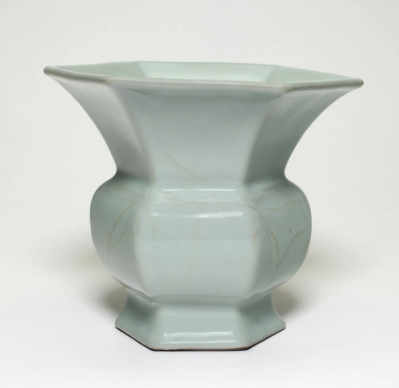 A pale celadon-glazed Chinese porcelain vase with a flaring hexagonal mouth and faceted body, photographed on a plain white ground.