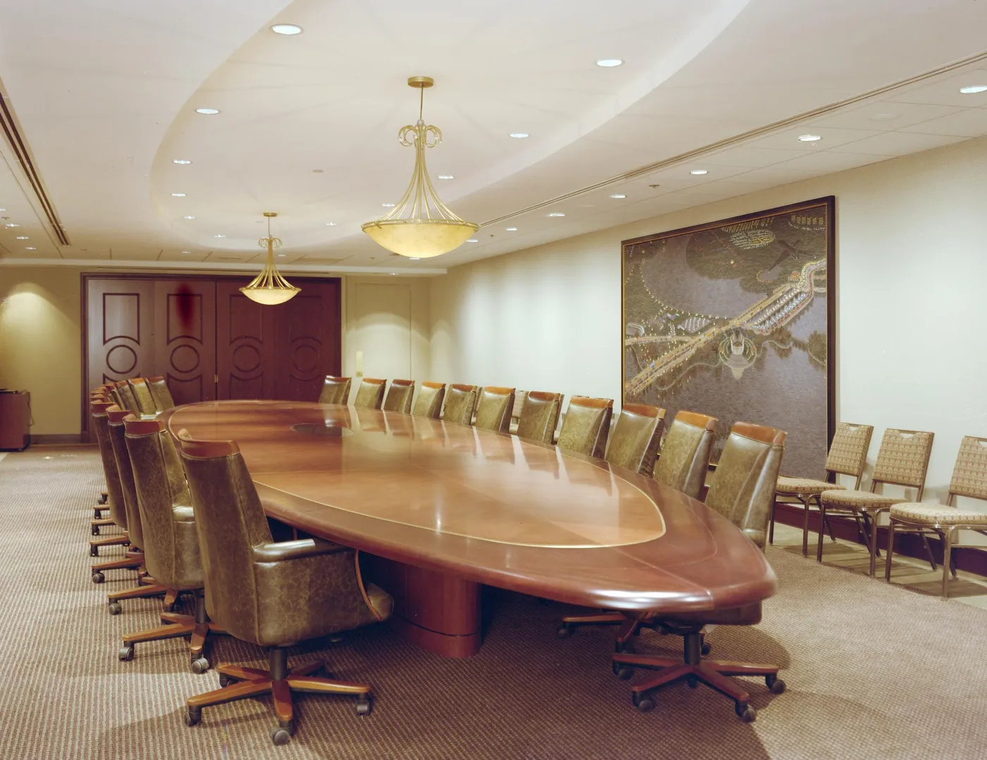 An empty boardroom with a long polished oval table ringed by leather chairs, alabaster pendant lights and a large framed map on the wall