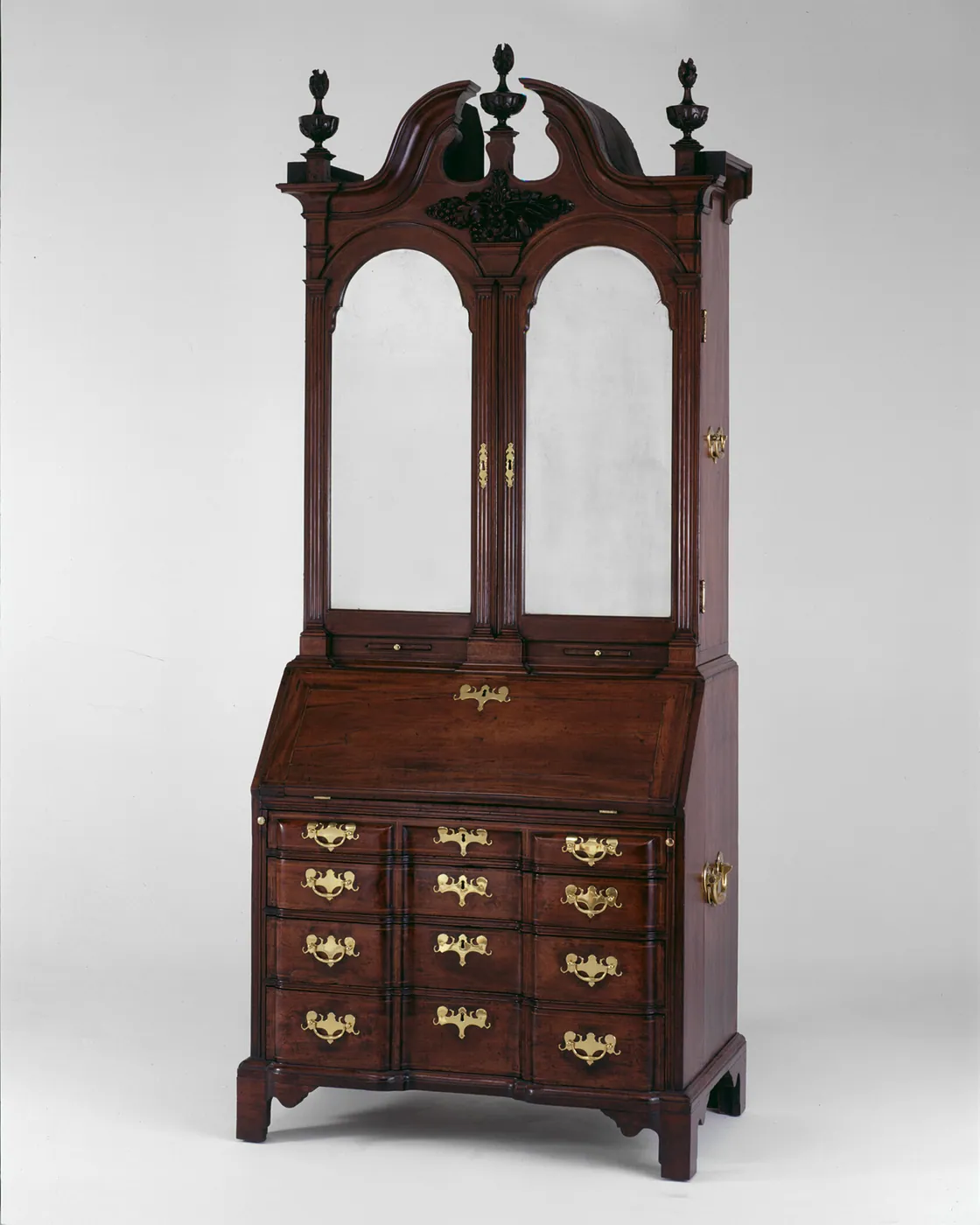An eighteenth-century mahogany desk and bookcase with a scrolled pediment, mirrored doors, a slant-front lid and brass-handled drawers.