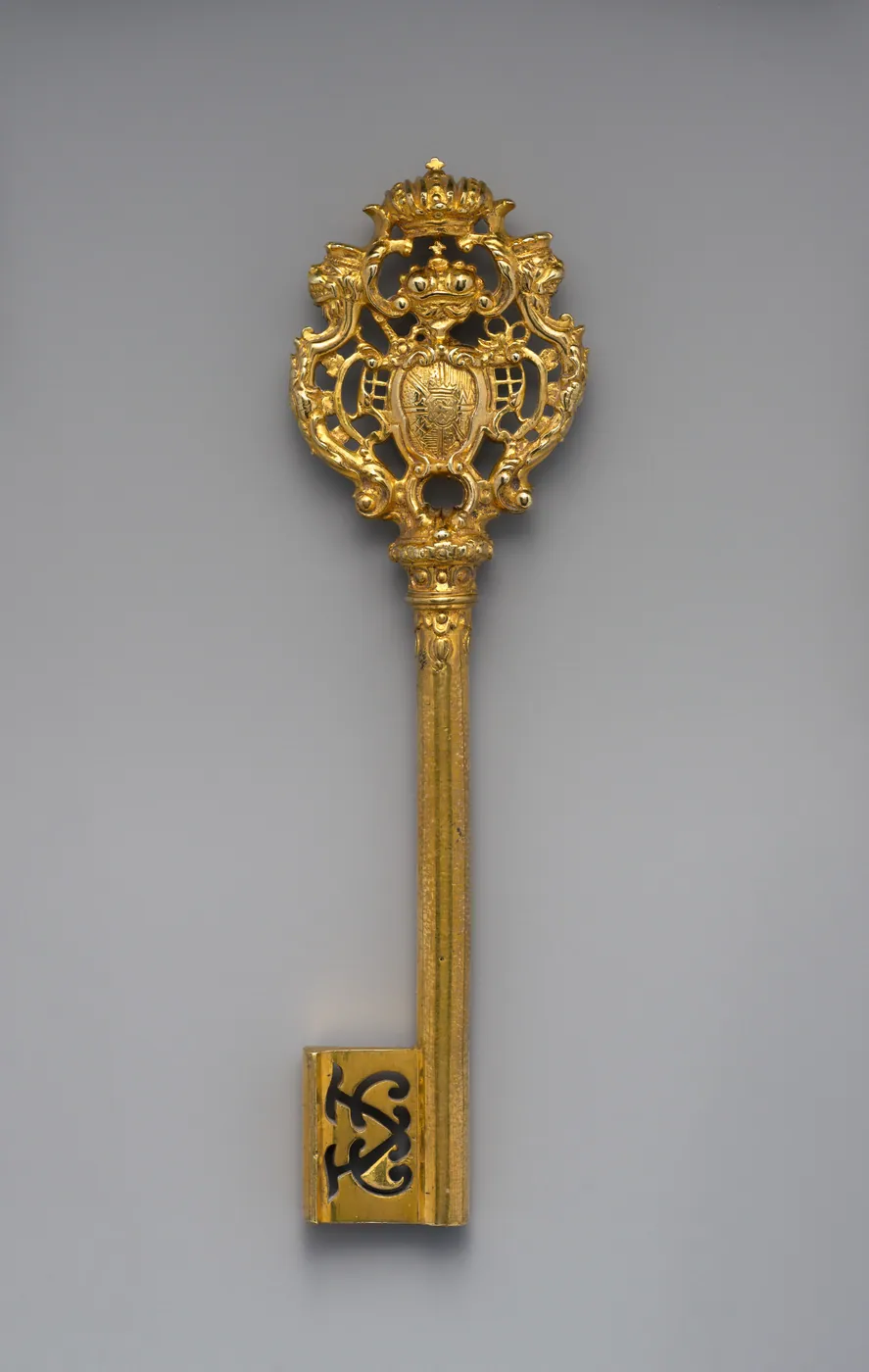 Gilded ceremonial key with an openwork crowned coat of arms at the bow, a fluted shaft and a monogrammed bit, on a grey ground