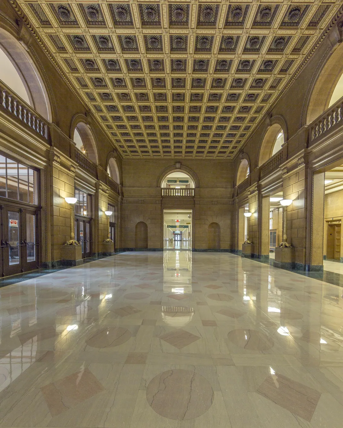 Empty grand hall inside the IRS Building with a coffered gilded ceiling, arched balconies and a polished marble floor reflecting the light