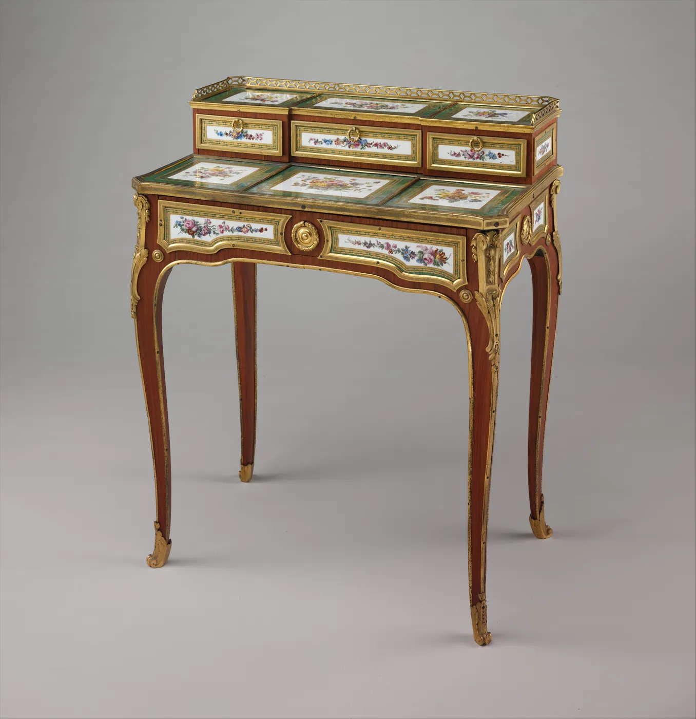 A small French writing desk on slender curved legs, set with painted porcelain flower plaques and gilt-bronze mounts