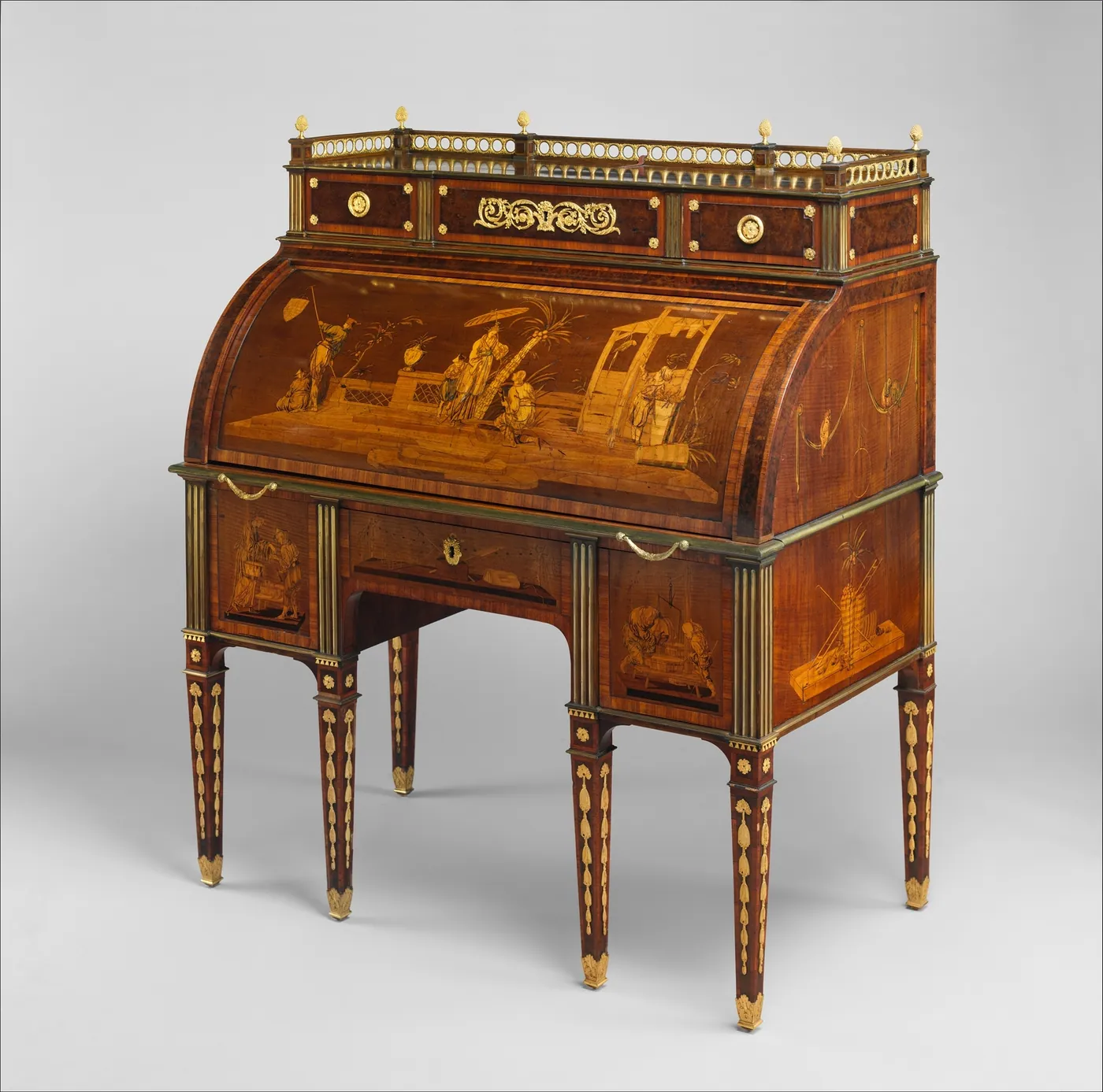 An eighteenth-century rolltop desk with pictorial marquetry, a brass-railed gallery, rows of small drawers and tapered legs, on grey