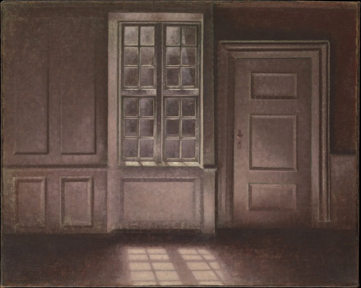 An empty paneled room in muted grays with a tall multi-paned window beside a closed door, pale light falling in squares across the floor.