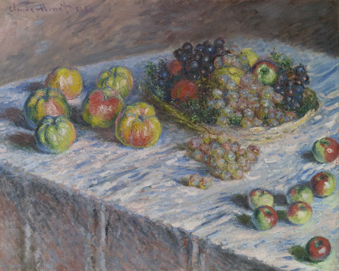 Apples scattered across a white tablecloth beside a basket heaped with green and purple grapes