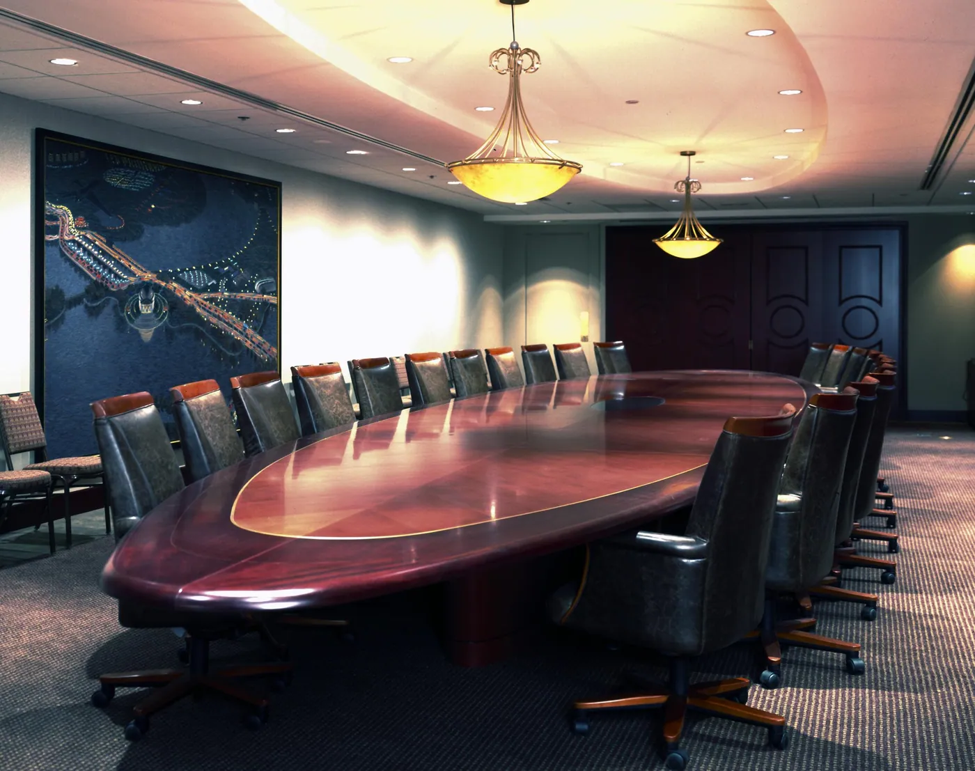 An empty boardroom with a long polished mahogany oval table, rows of leather chairs and warm pendant lights.