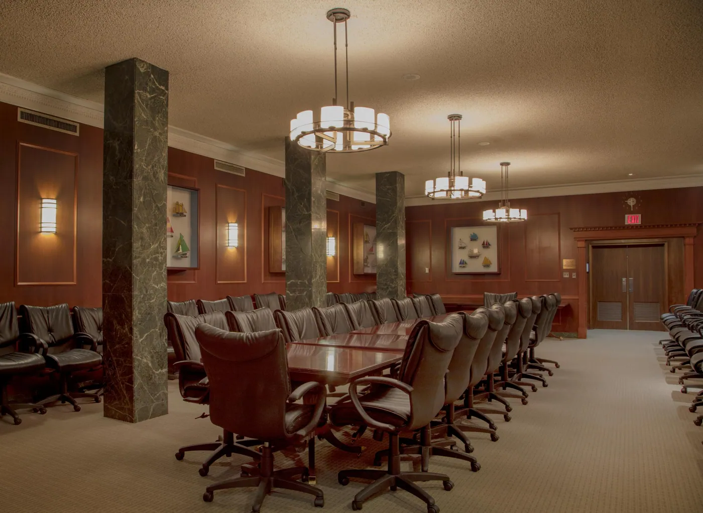 A long polished conference table ringed with leather chairs in a wood-panelled room with marble columns and pendant lights