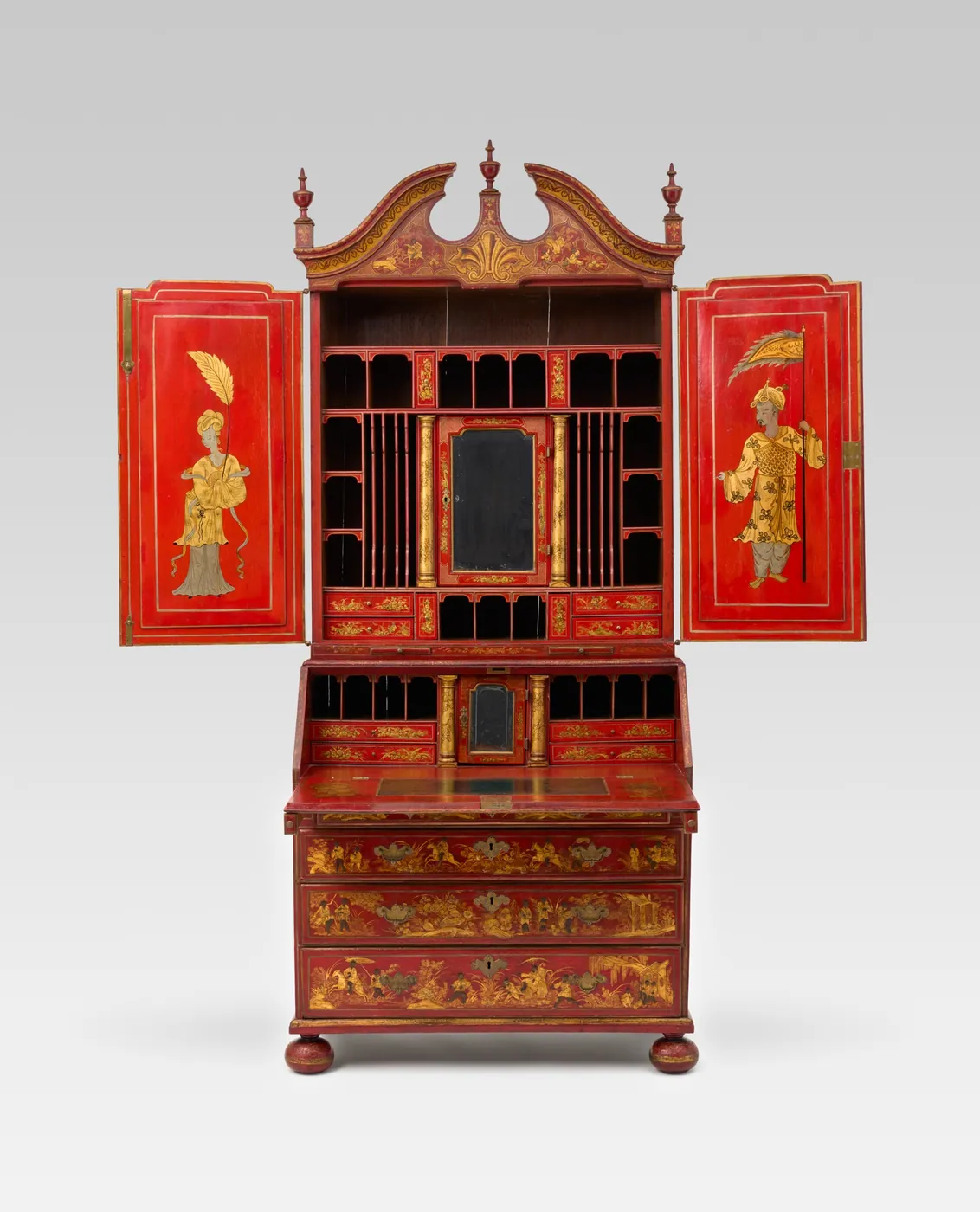 A red-lacquered Georgian bureau secretary with gilt decoration, its upper doors open to show rows of pigeonholes, small drawers and a fall-front writing surface.