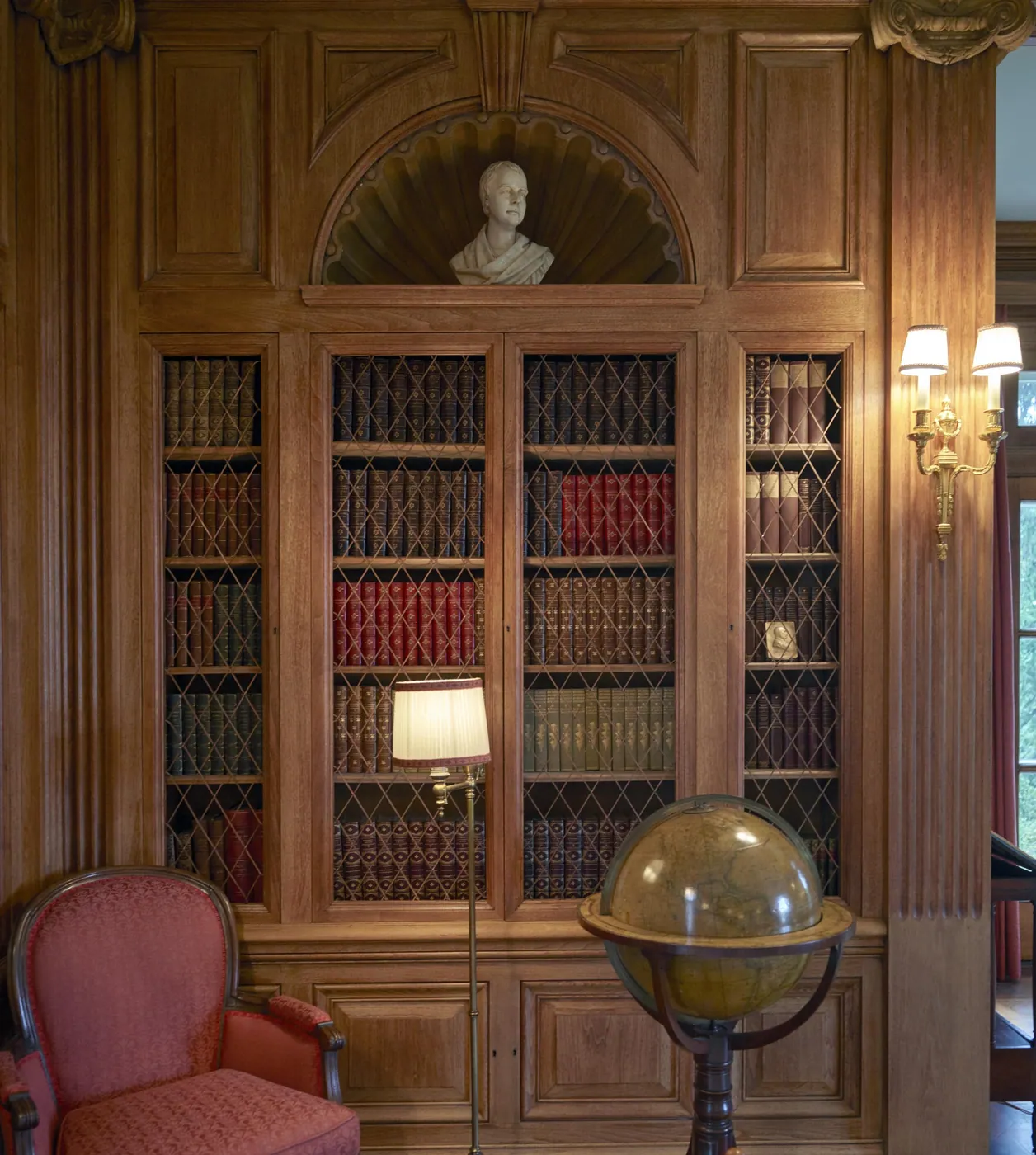 Oak-panelled study with lattice-fronted bookcases, a reading lamp, an antique globe on a stand and a coral armchair