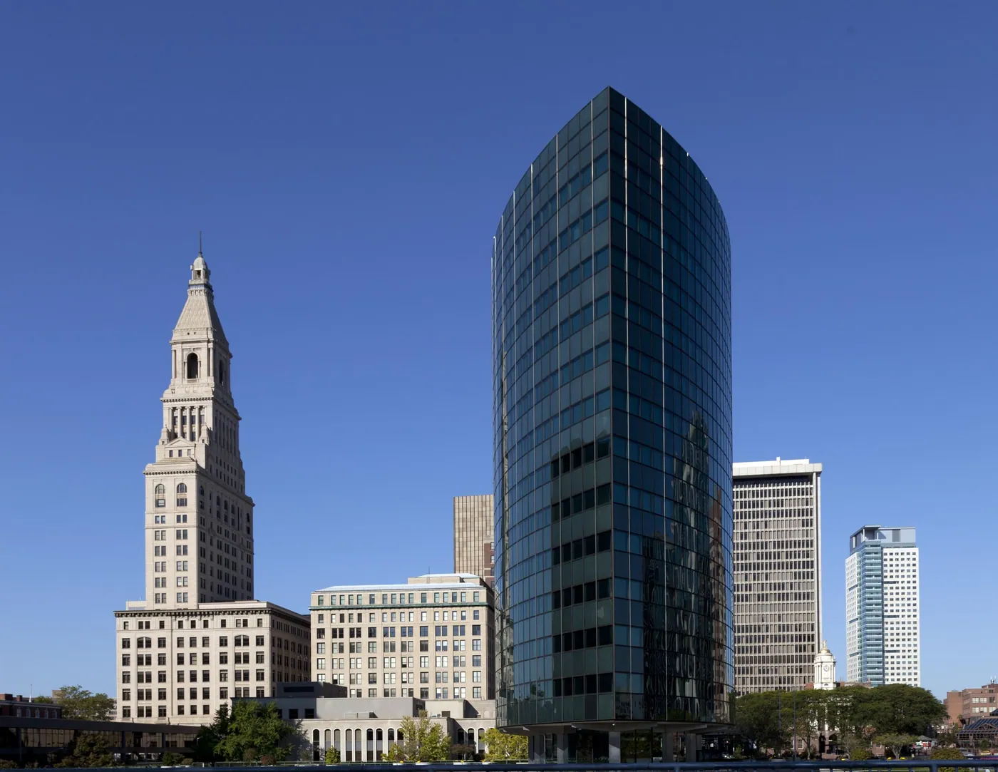 The Travelers Tower beside a curved dark-glass office tower and other downtown buildings against a deep blue sky.