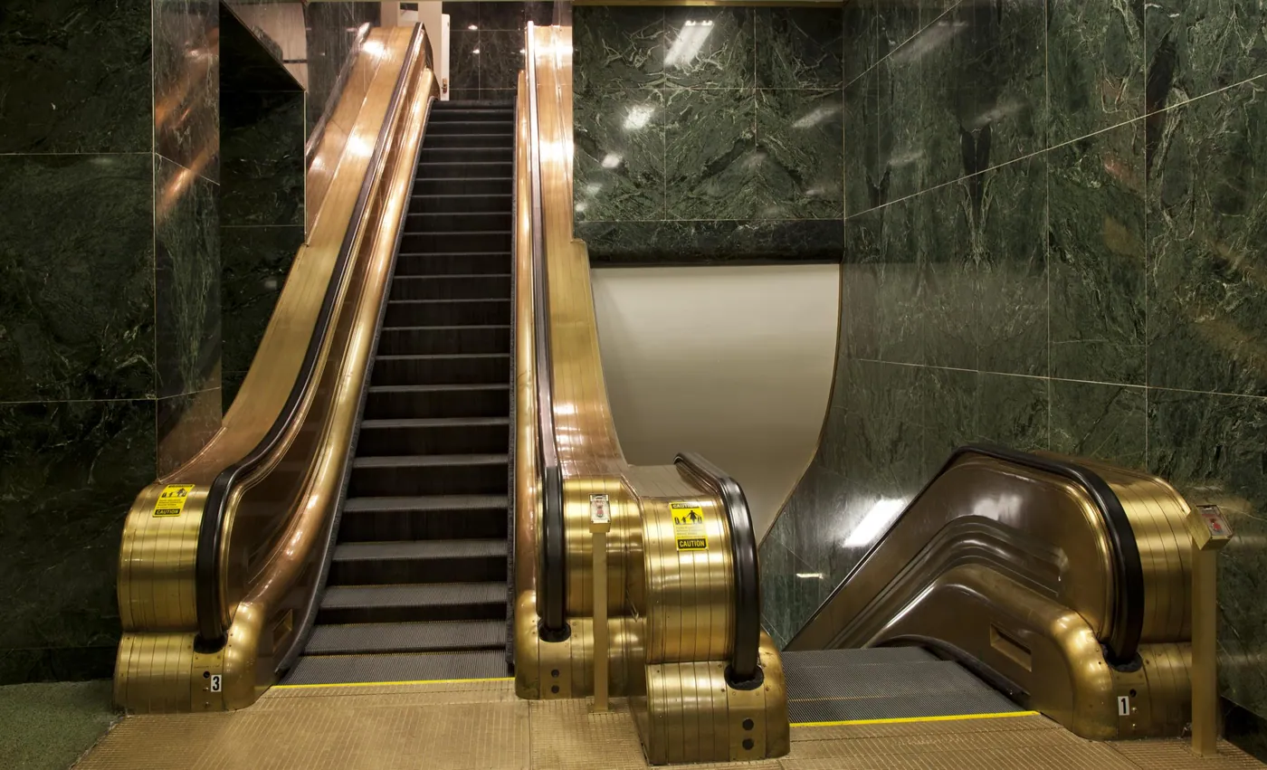Bronze-clad escalators rising between walls of polished dark green marble inside a Washington federal office building