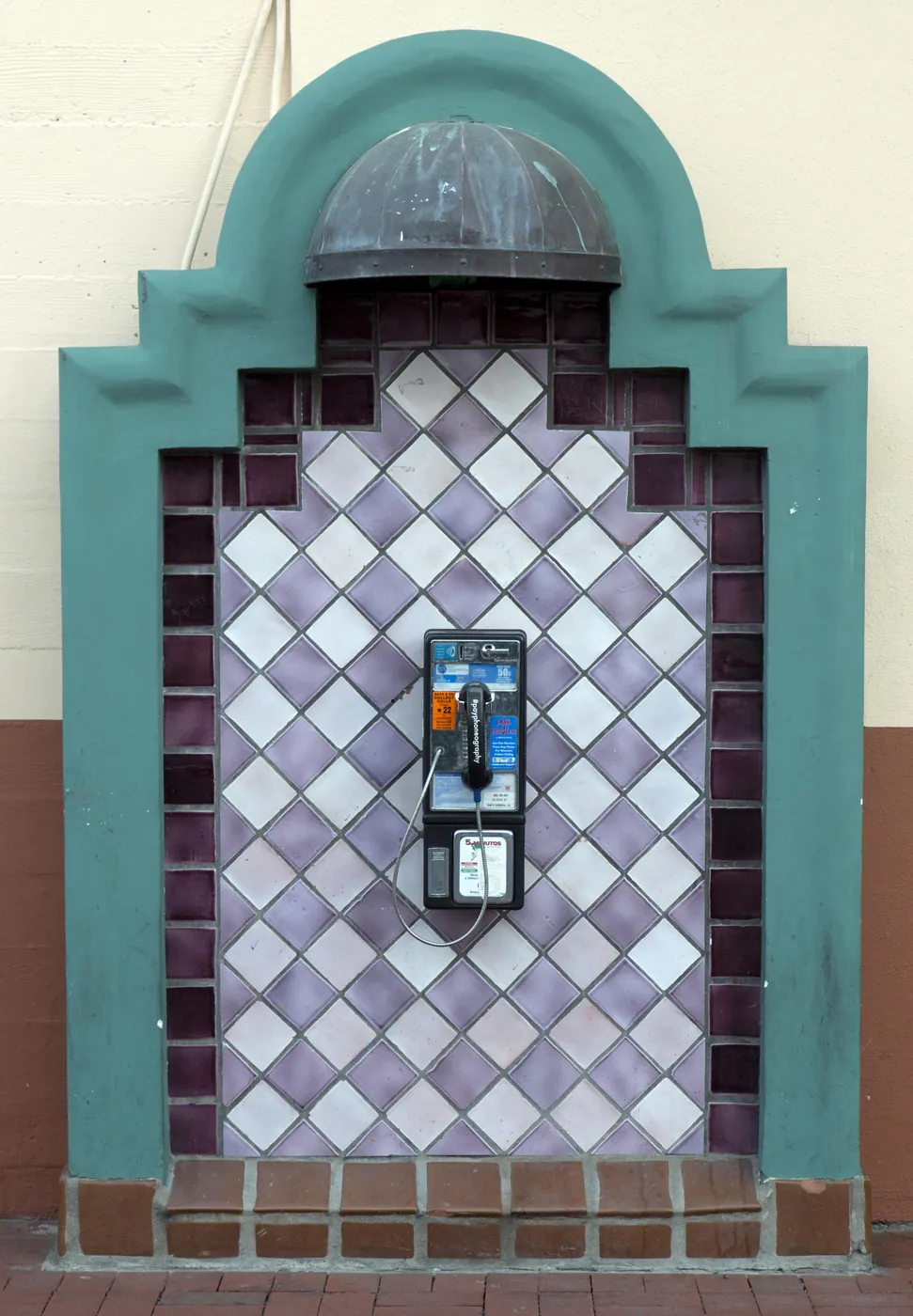 A telephone set into an arched alcove of violet and white diamond tiles with a teal surround and a small copper hood