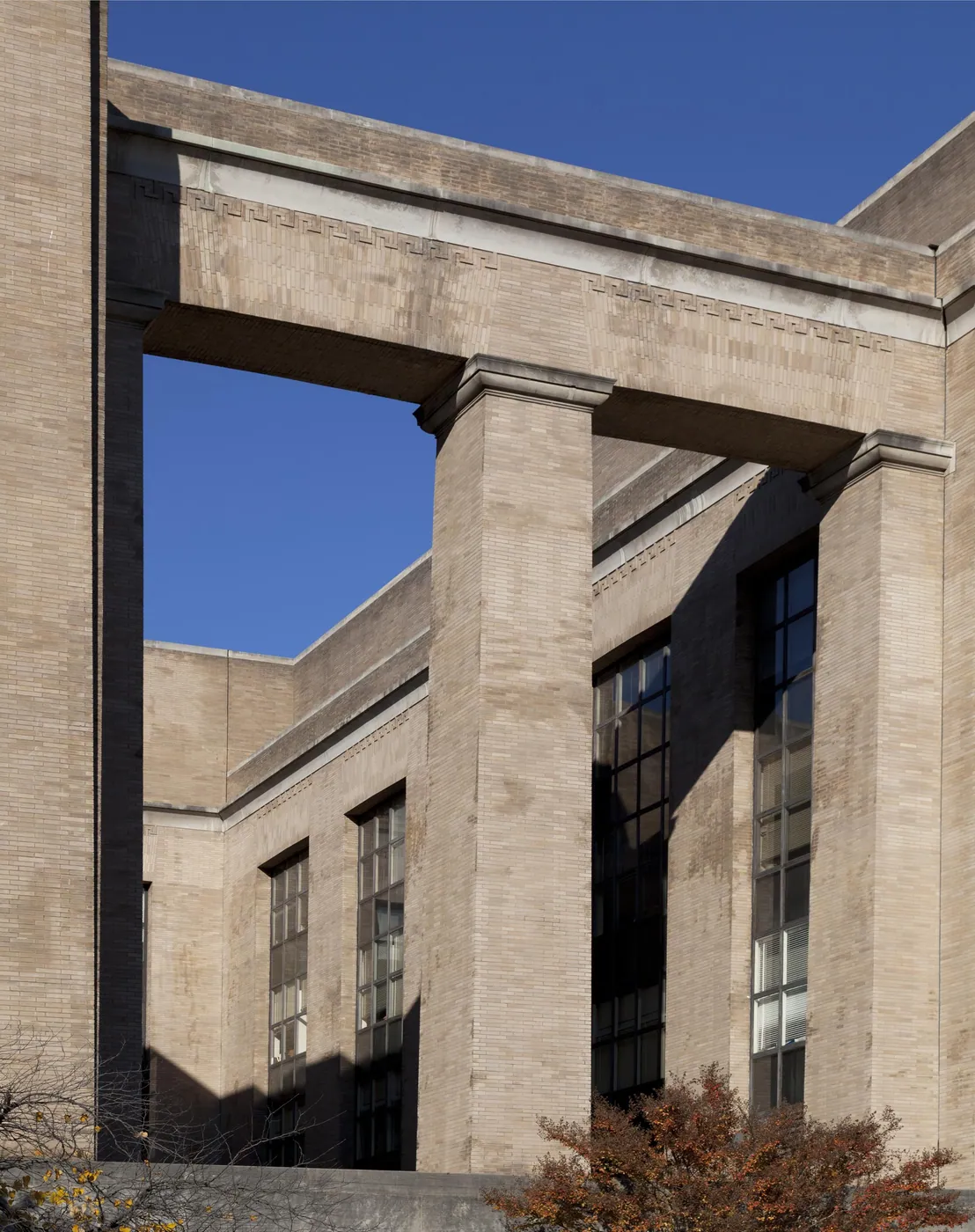 Tall square limestone piers and a Greek-key lintel of a stripped-classical federal building against a deep blue sky, with autumn foliage below