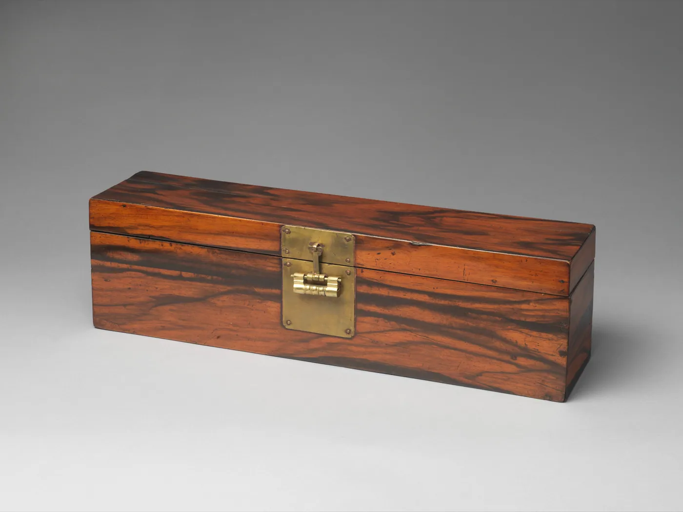 A long, narrow persimmon-wood document box with a richly figured grain and a square brass lock plate on its front