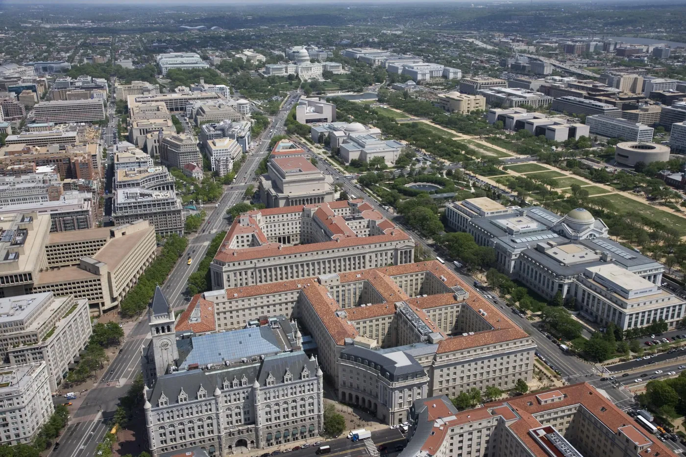 Aerial view of the red-tiled federal office buildings of the Federal Triangle along Pennsylvania Avenue, with the Capitol dome in the distance