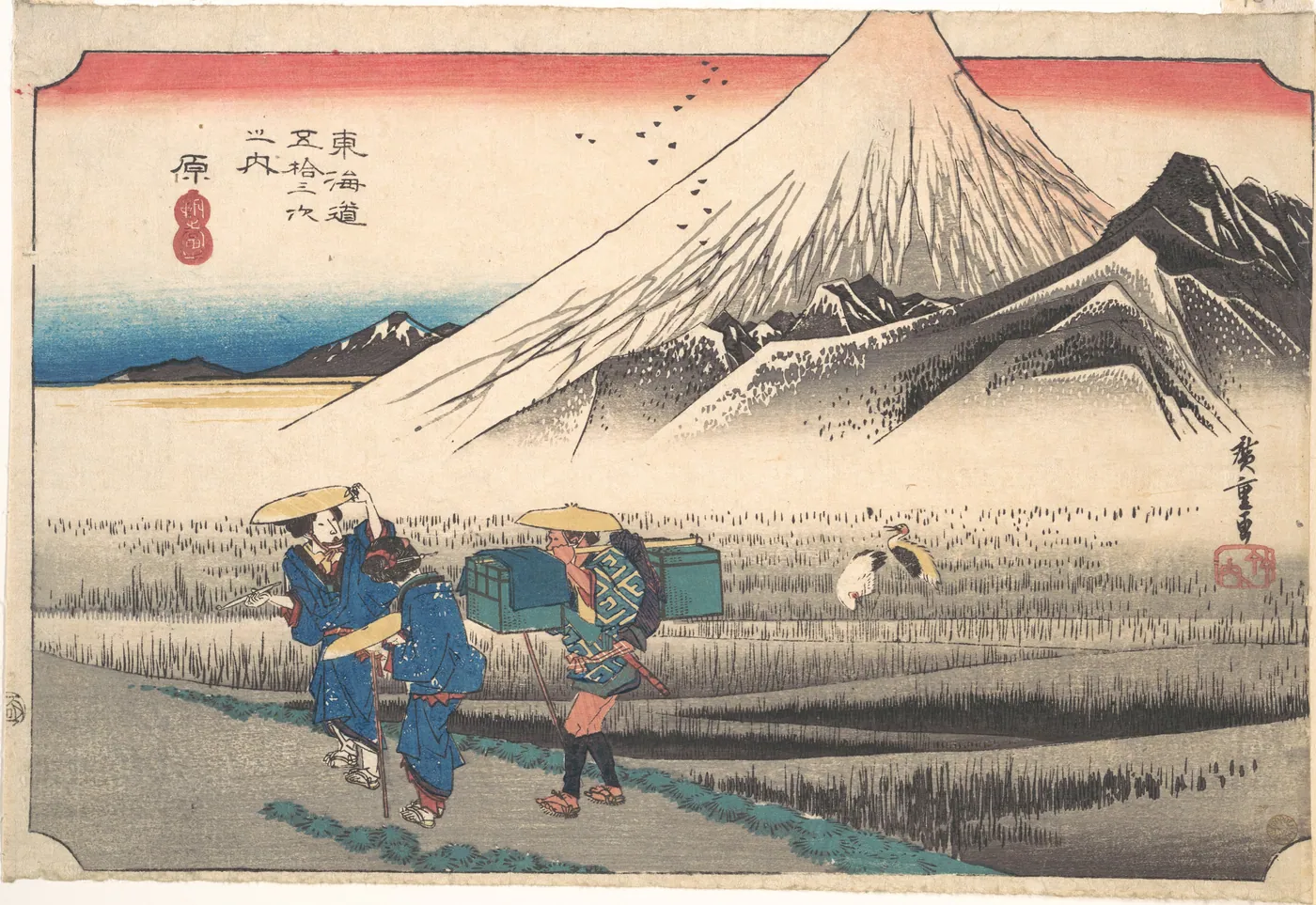 Woodblock print of two women travellers and a porter carrying luggage boxes along a road past rice fields, with Mount Fuji rising above the frame