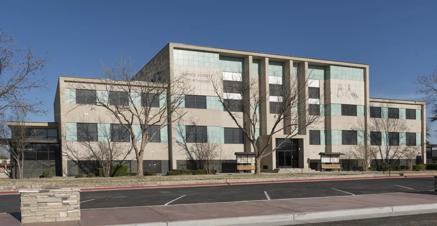 A four-storey mid-century modernist county courthouse with stone piers and pale green panels, bare trees in front under a clear blue sky