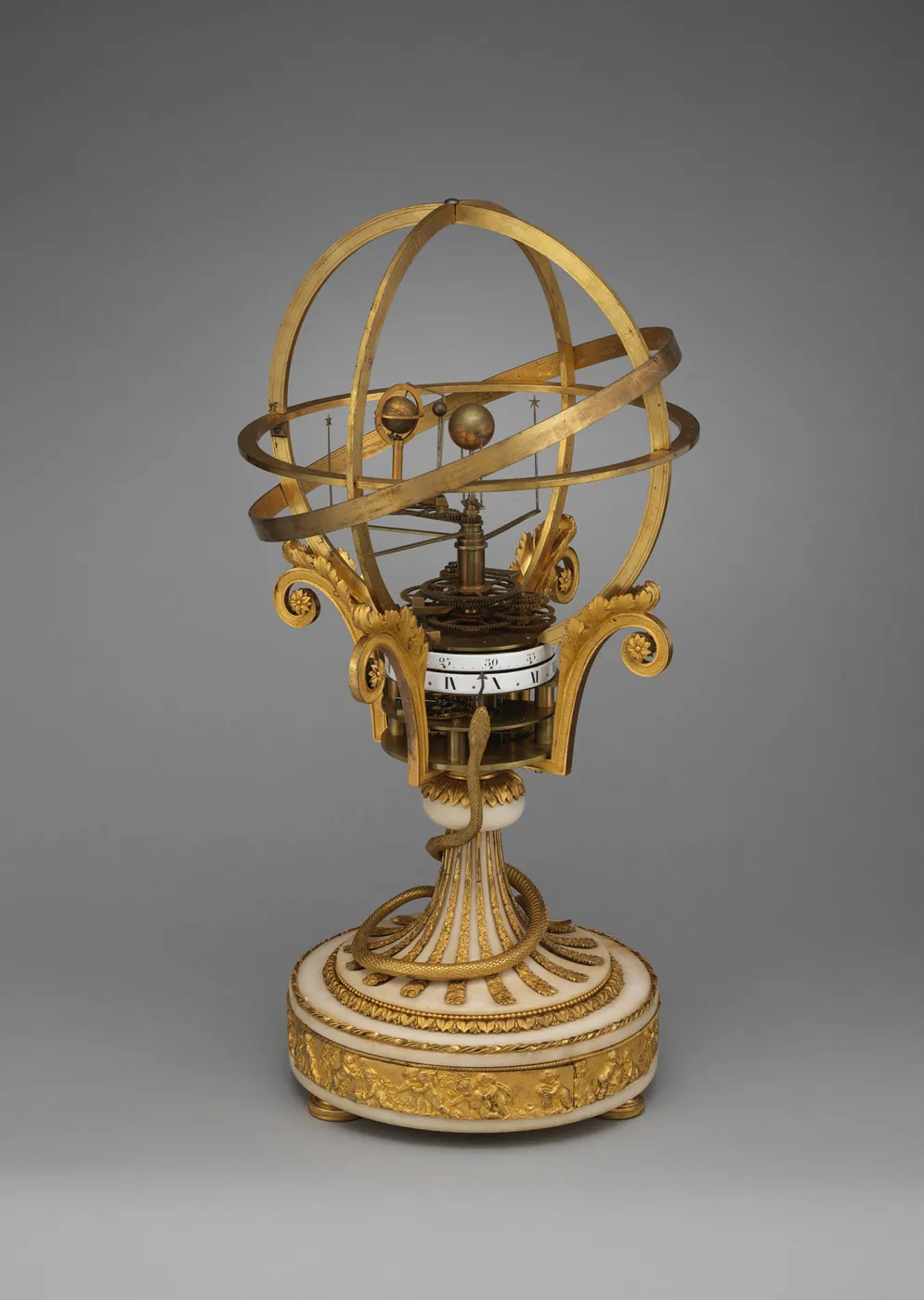 A gilt-bronze orrery clock with open armillary rings and small planet spheres over a clock dial, on a fluted white marble base.