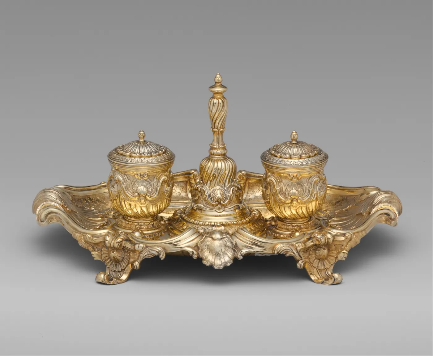 Gilded rococo inkstand on scrolled feet, with two lidded ink pots on either side of a tall twisted handbell on a shell-edged tray