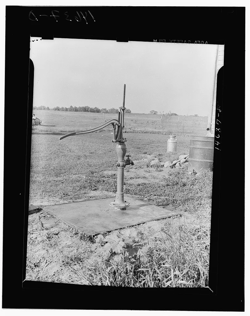 A metal hand pump stands over a capped well in a Minnesota field in 1941