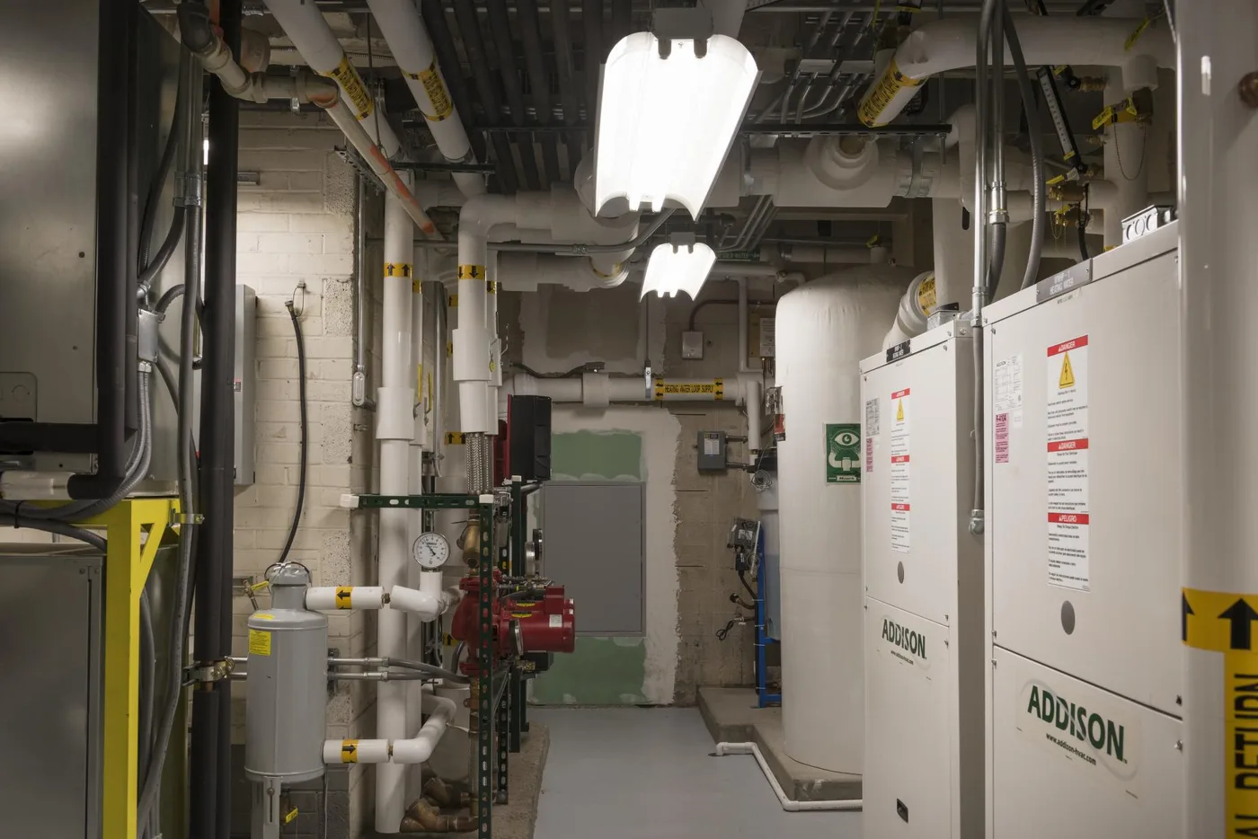 Pipes, gauges, electrical panels, and mechanical equipment in a brightly lit basement room