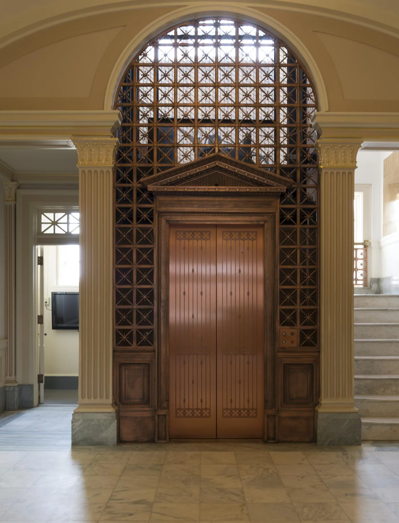 An ornate copper-colored elevator stands inside a historic Texas building