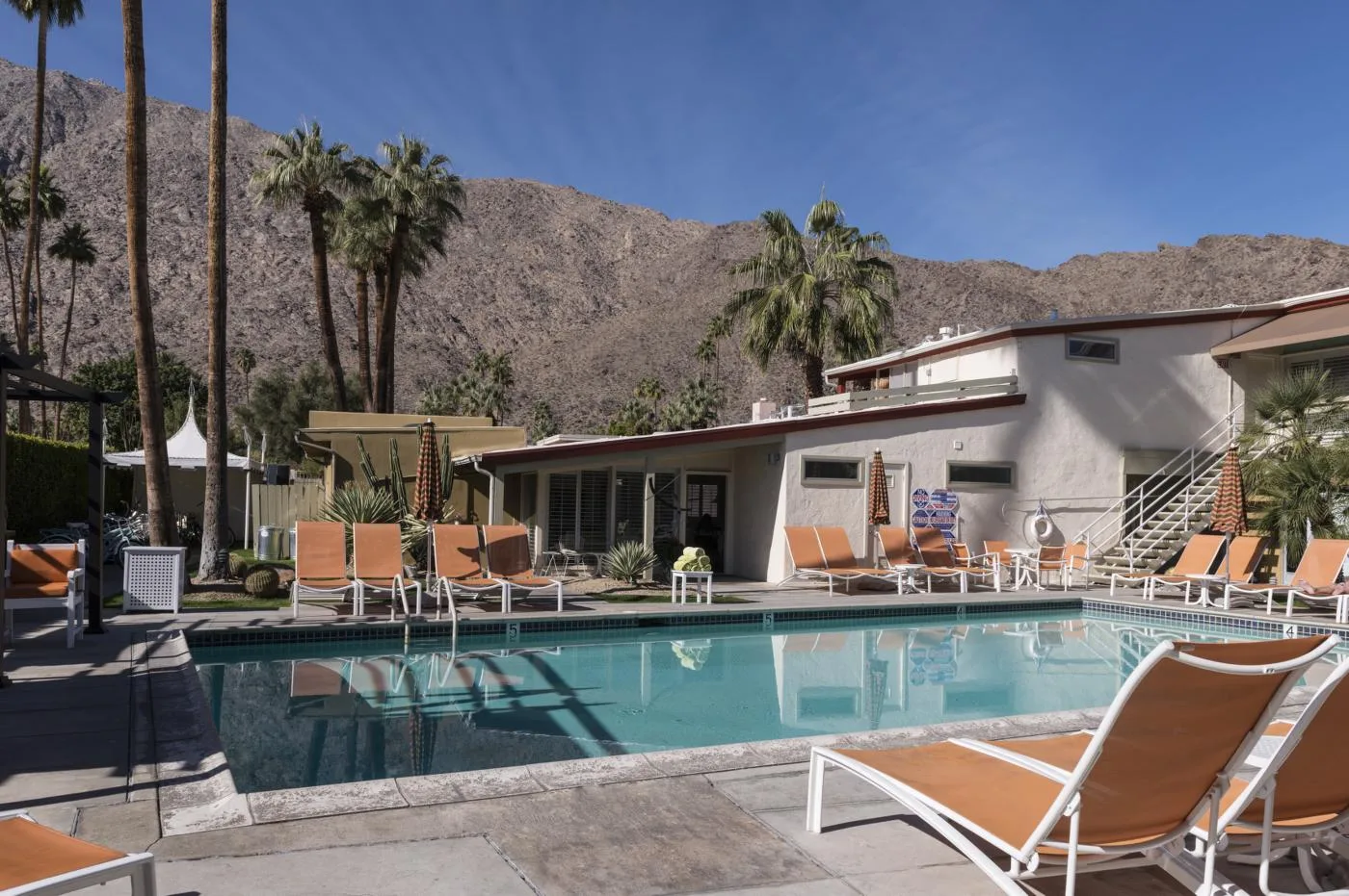 A turquoise outdoor swimming pool and lounge chairs sit below the mountains in Palm Springs