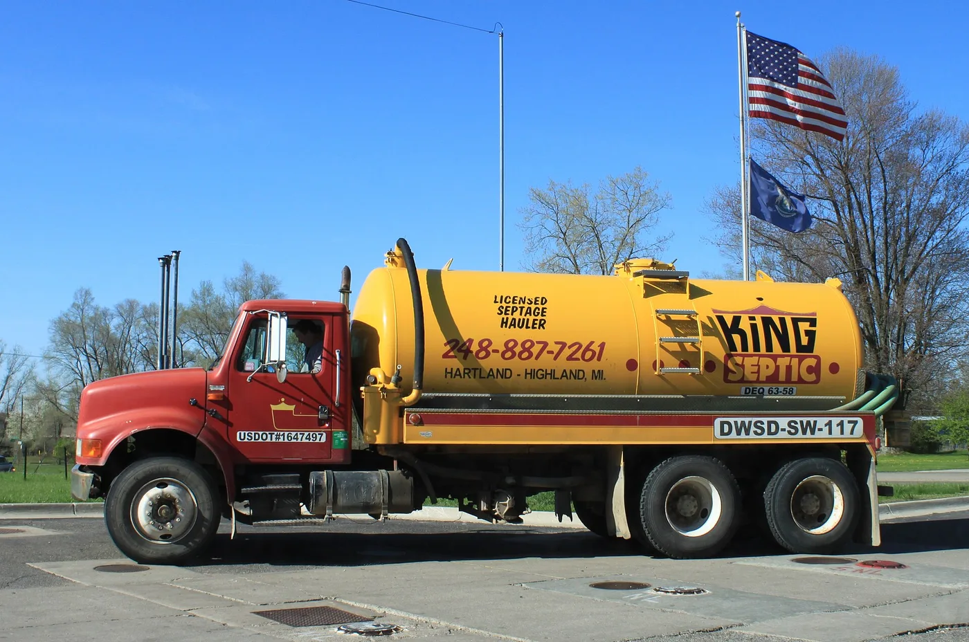 A red and yellow licensed septage pump truck parked under a clear blue sky