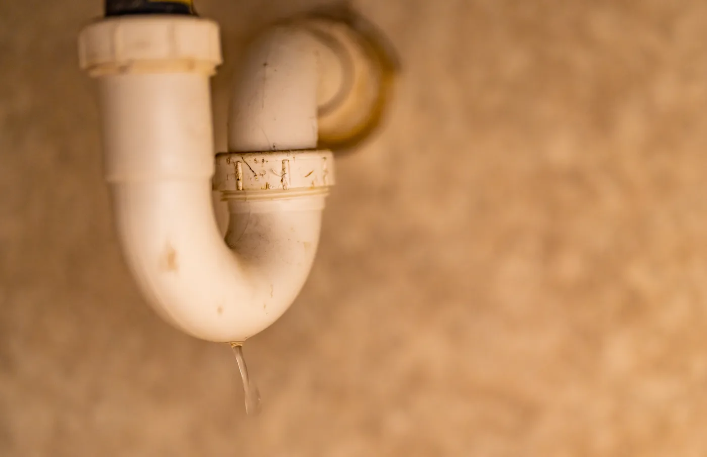 A clear stream of water dripping from the joint of a white plastic sink drain trap