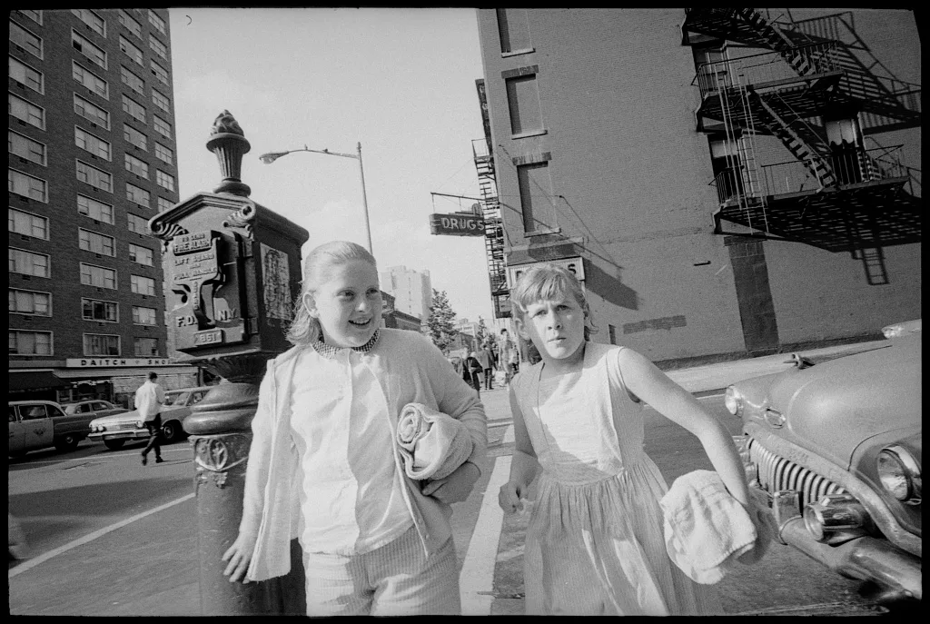 Two girls stand beside a cast-iron street fire-alarm box in New York in 1964